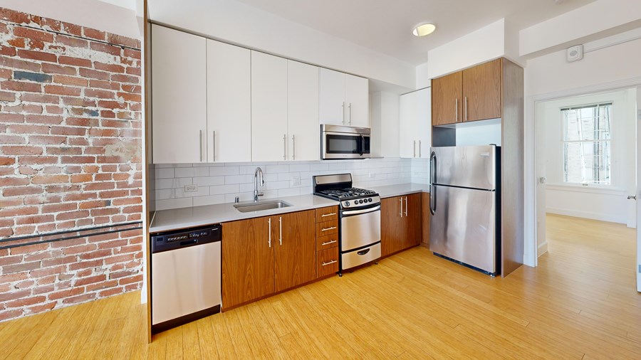 A kitchen with a brick wall and wooden floors.